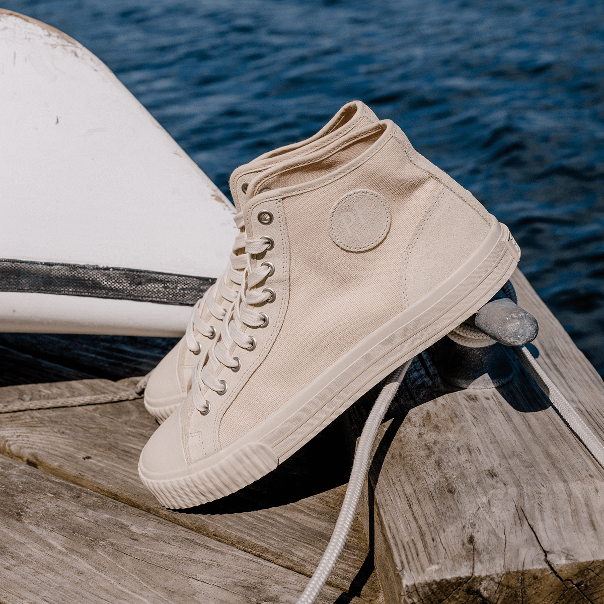 Beige high-top sneakers on a wooden surface with water in the background.
