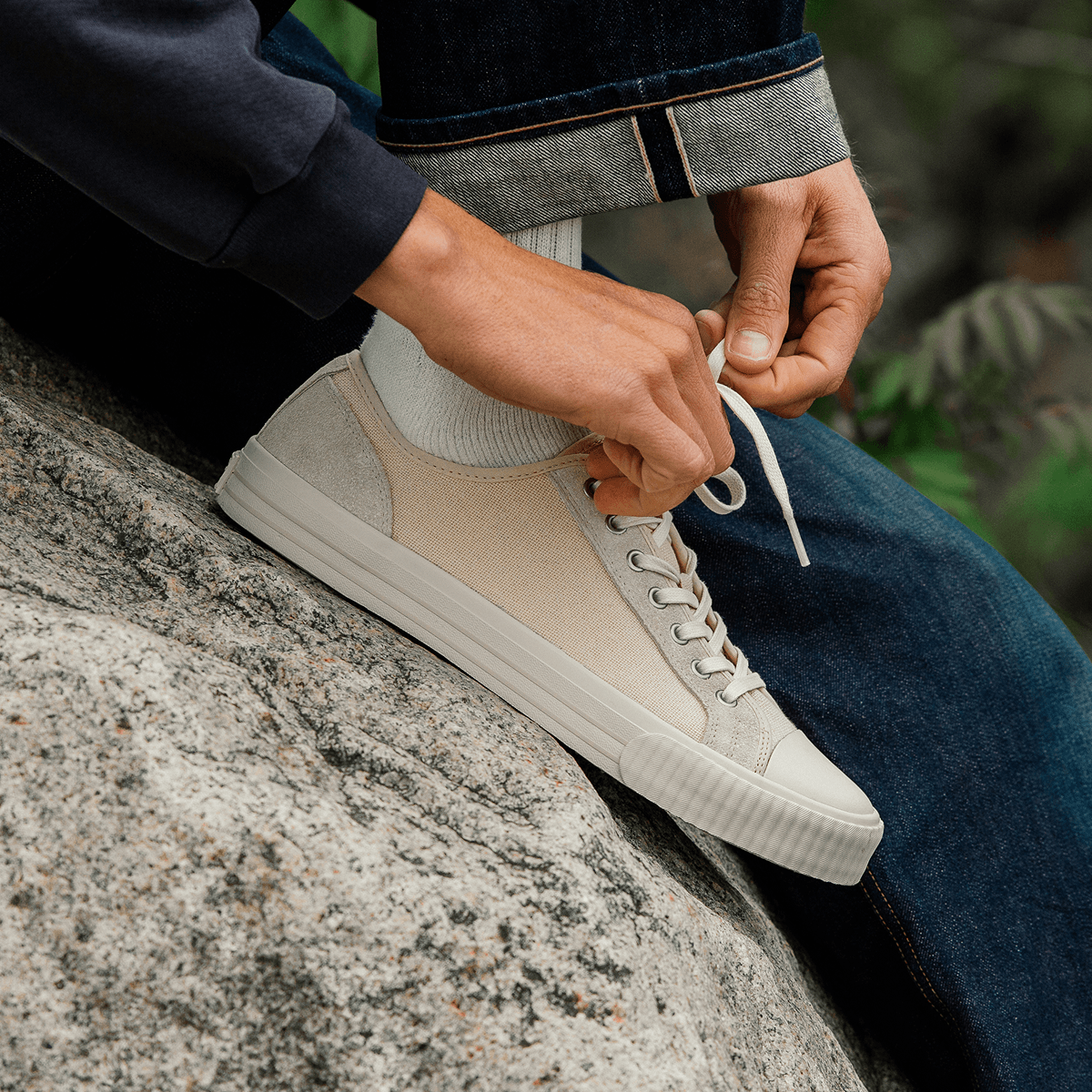Person tying shoelaces on a beige low-top sneaker outdoors.