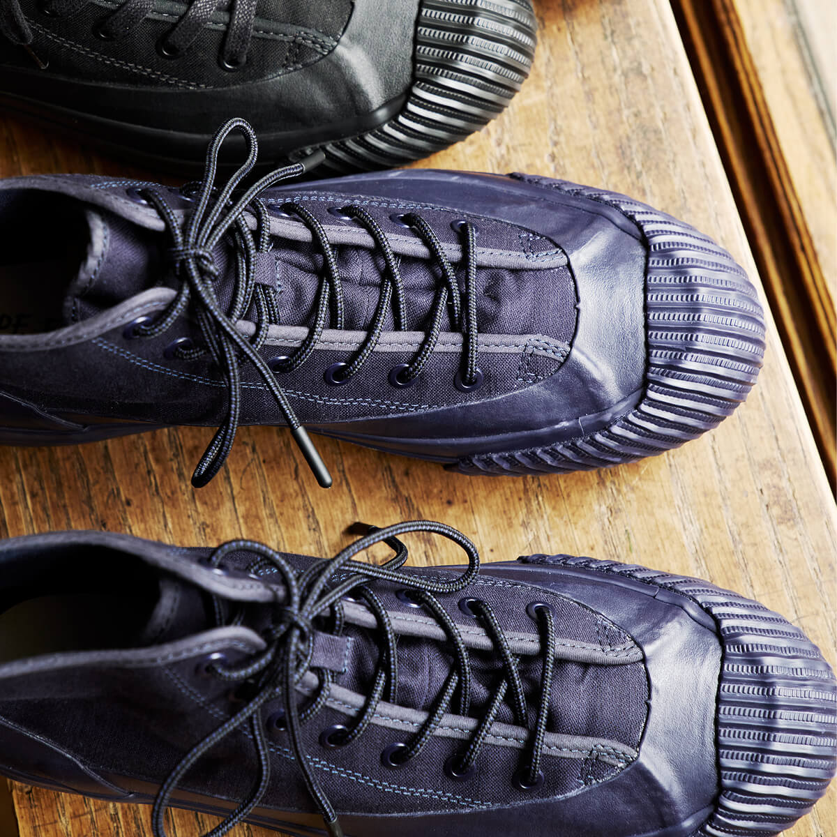 A pair of navy boots with lugged rubber outsoles and round hiker laces arranged on a wooden surface.