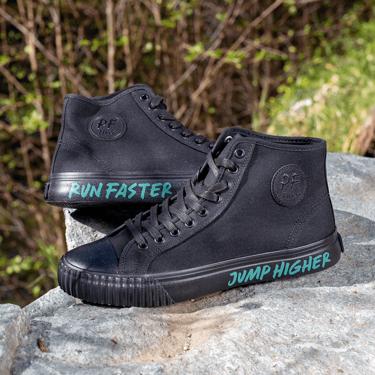 Black high-top sneakers with the phrases 'Run Faster' and 'Jump Higher' placed on a rock surrounded by green foliage.