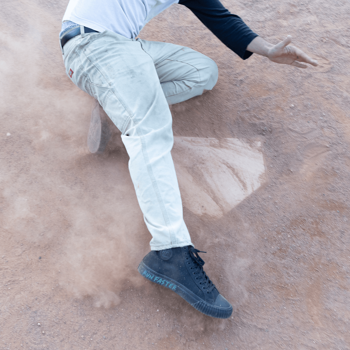 Person sliding on a field wearing black high-top shoes.