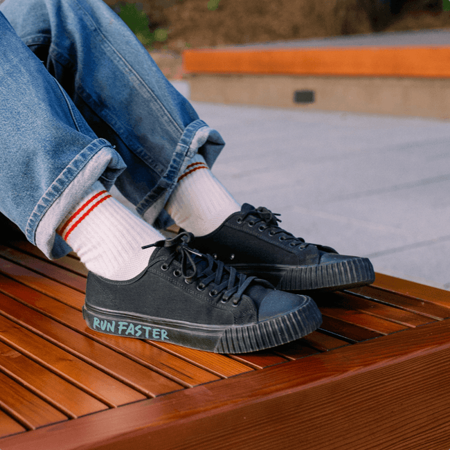 Person wearing black low-top sneakers with 'Run Faster' text, sitting on a wooden bench.