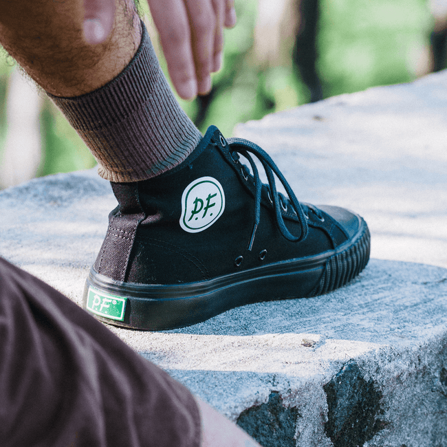 Person wearing a black high-top sneaker on a stone surface.
