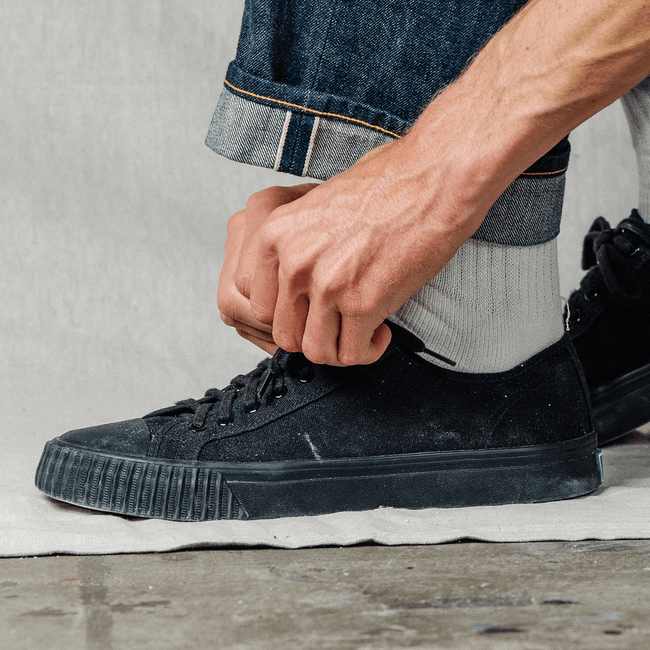 Person tying the laces of a black low-top sneaker.