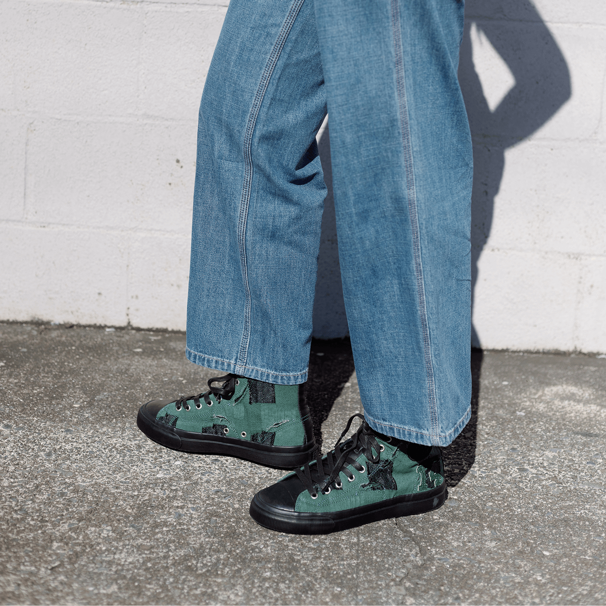 Person wearing green high-top sneakers and blue jeans against a white wall.