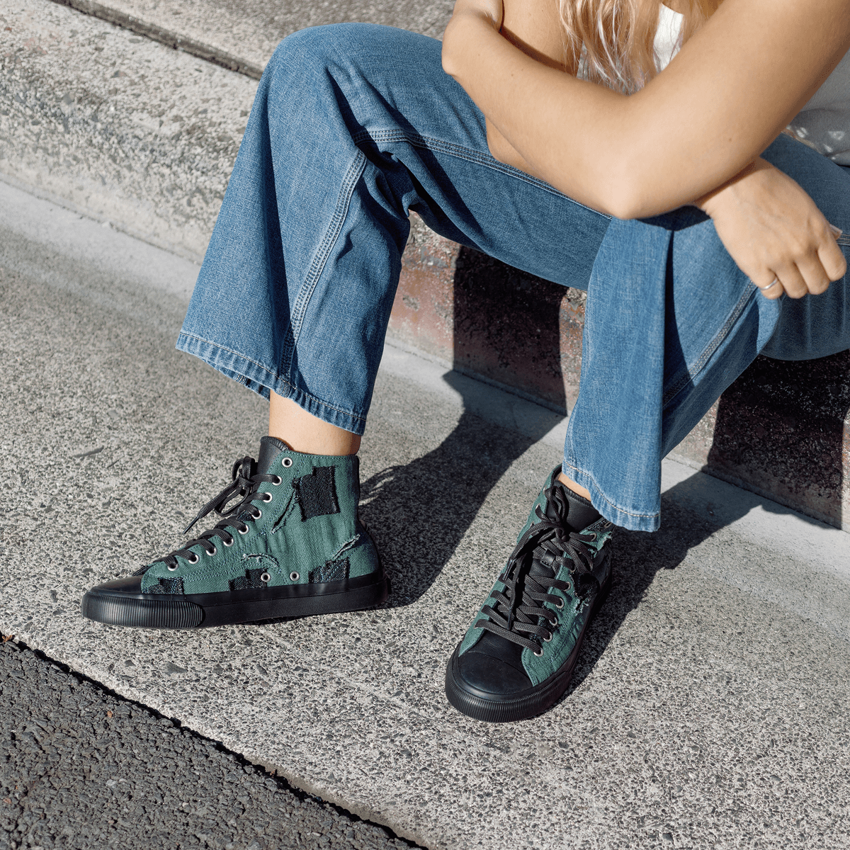 Person wearing green high-top sneakers sitting on a curb.