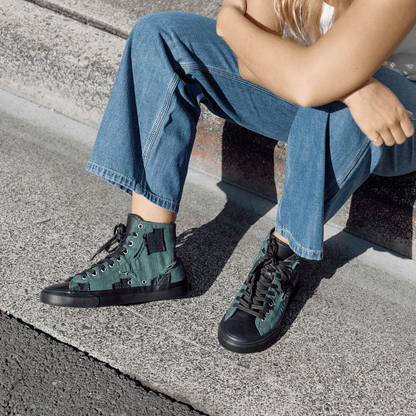 Person wearing green high-top sneakers sitting on a curb.