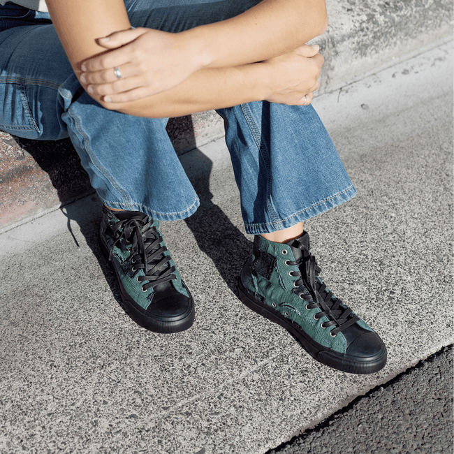 Person wearing green high-top sneakers with black soles while sitting on a curb.