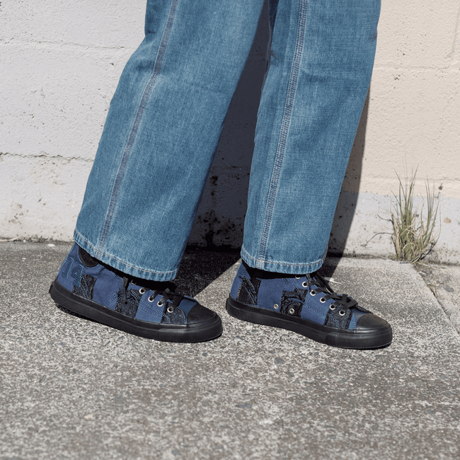 Person wearing blue jeans and navy high-top sneakers with black soles on a sidewalk.