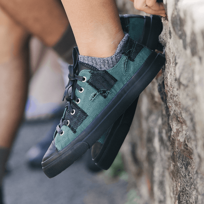 Green and black low-top sneakers worn by a person sitting a stone wall.