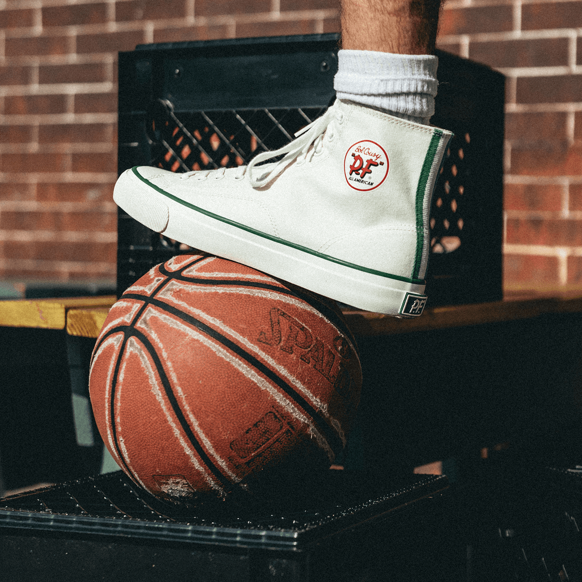 Person propping their foot on a basketball while wearing a white high-top sneaker with green accents.