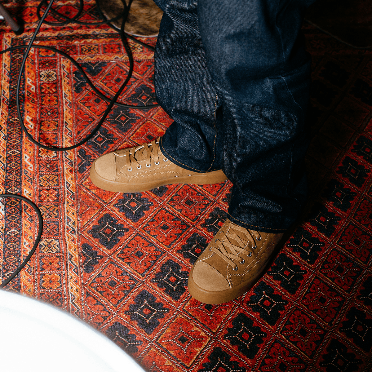 Person wearing tan high-top sneakers and blue jeans while standing on a patterned rug.
