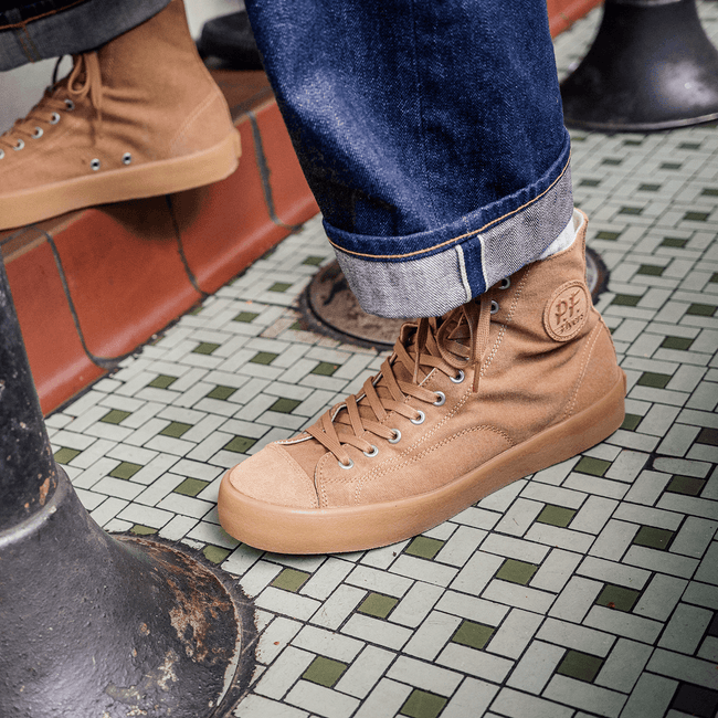 Tan high-top sneakers worn on a tiled floor.