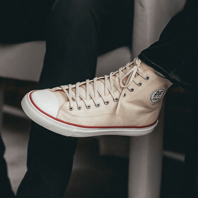 Close up of a white high-top sneaker with red accents worn by a person.