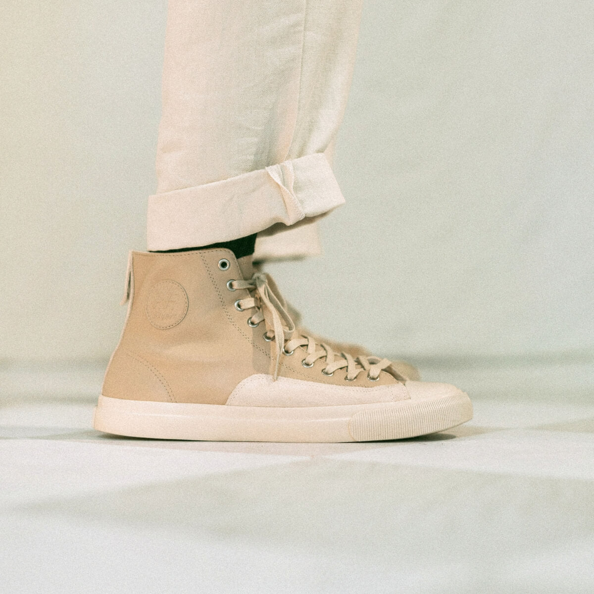 Beige high-top sneakers worn with light-colored pants on a neutral background