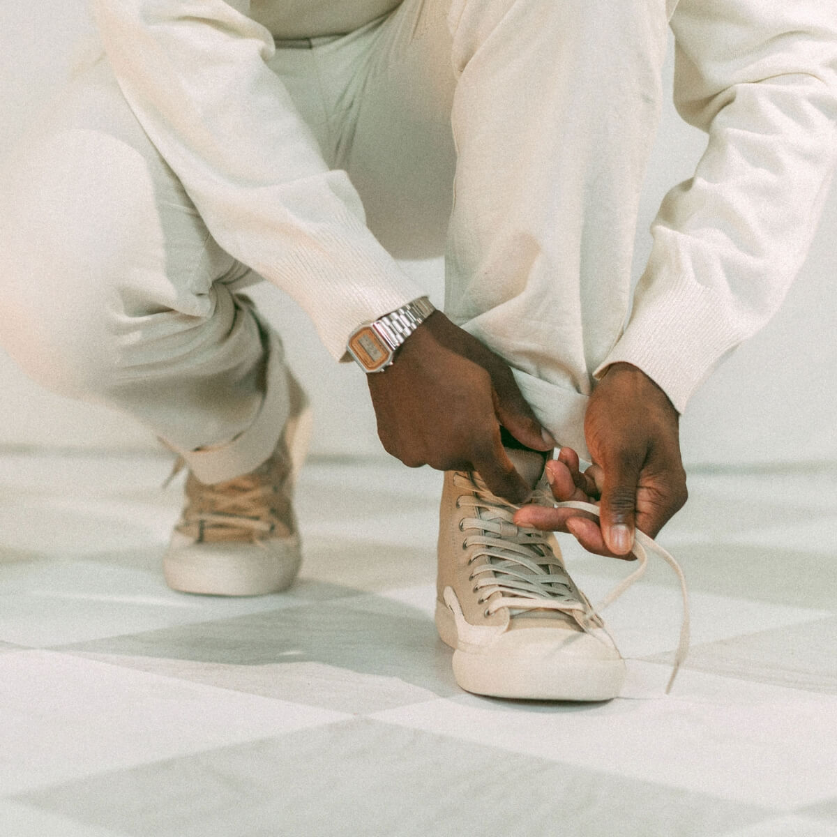 Person tying a taupe sneaker on a light background