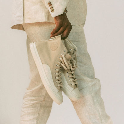 Person wearing a beige suit holding a beige sneaker against a neutral background