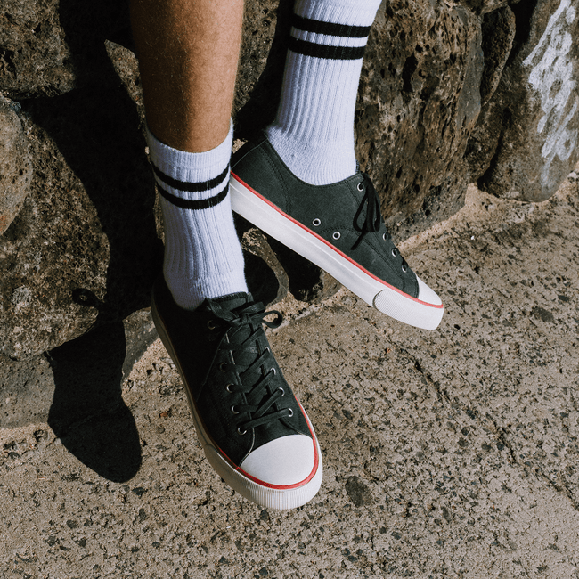 Person sitting on a stone wearing white ankle socks and black low-top sneakers with red accents.