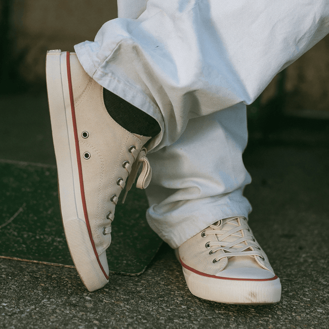 White low-top sneakers with red accents worn with white baggy jeans on a concrete surface.