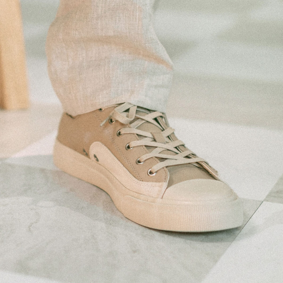 Beige sneaker worn with light-colored pants on a neutral background
