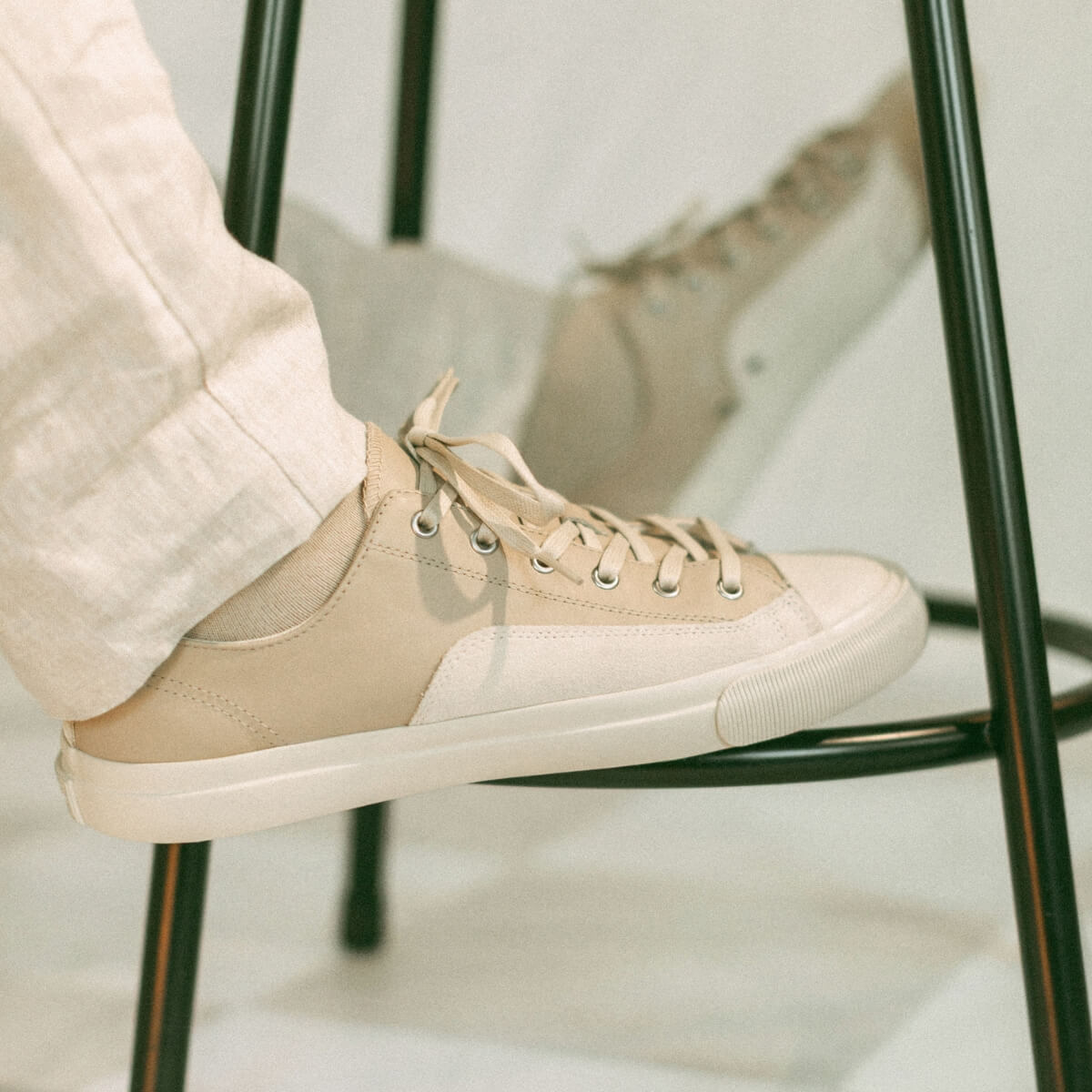 Beige sneaker worn with light-colored pants on a chair.