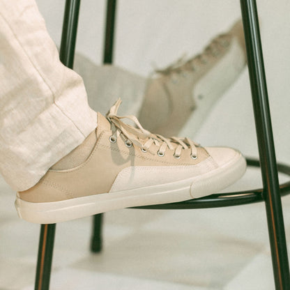 Beige sneaker worn with light-colored pants on a chair.