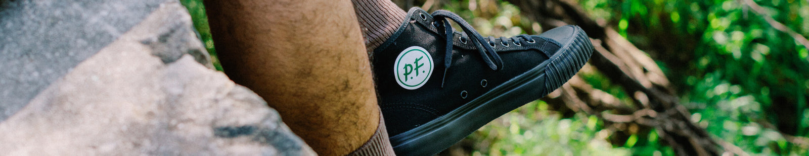 Black high-top sneaker with a 'P.F. Flyers' logo on a blurred natural background.