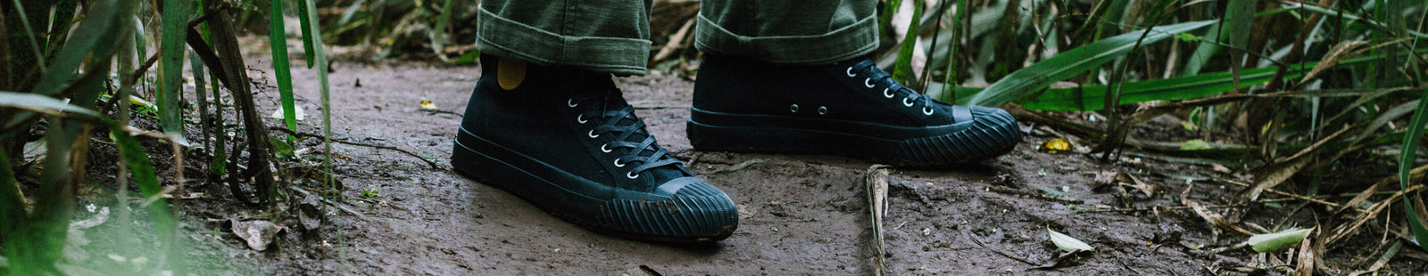 Person wearing black high-top sneakers on a muddy path.
