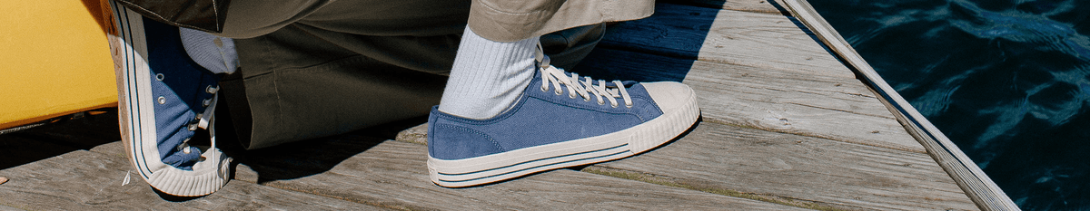 Indigo blue low-top sneakers worn on a wooden dock.