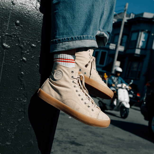 Beige high-top sneakers with tan soles worn by a person on a street.