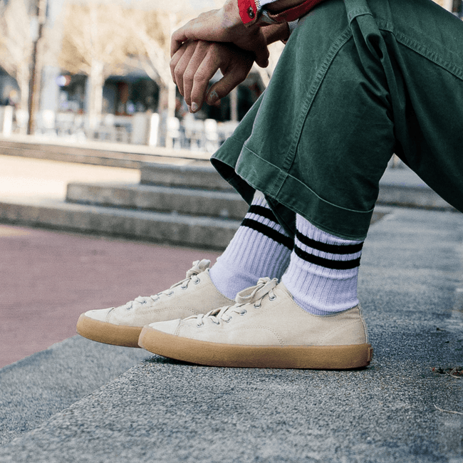 Person sitting on a concrete ledge wearing green pants and beige low-top sneakers in an urban setting.