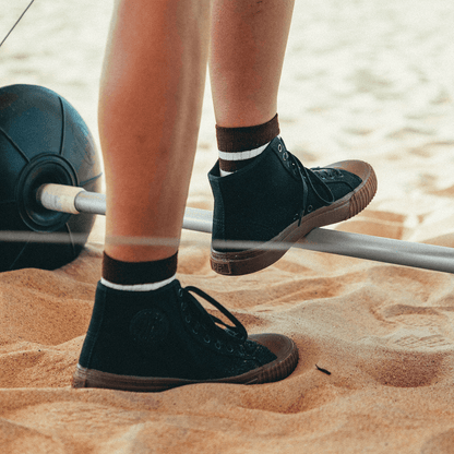 Person standing on sand wearing brown pants and black high-top shoes.