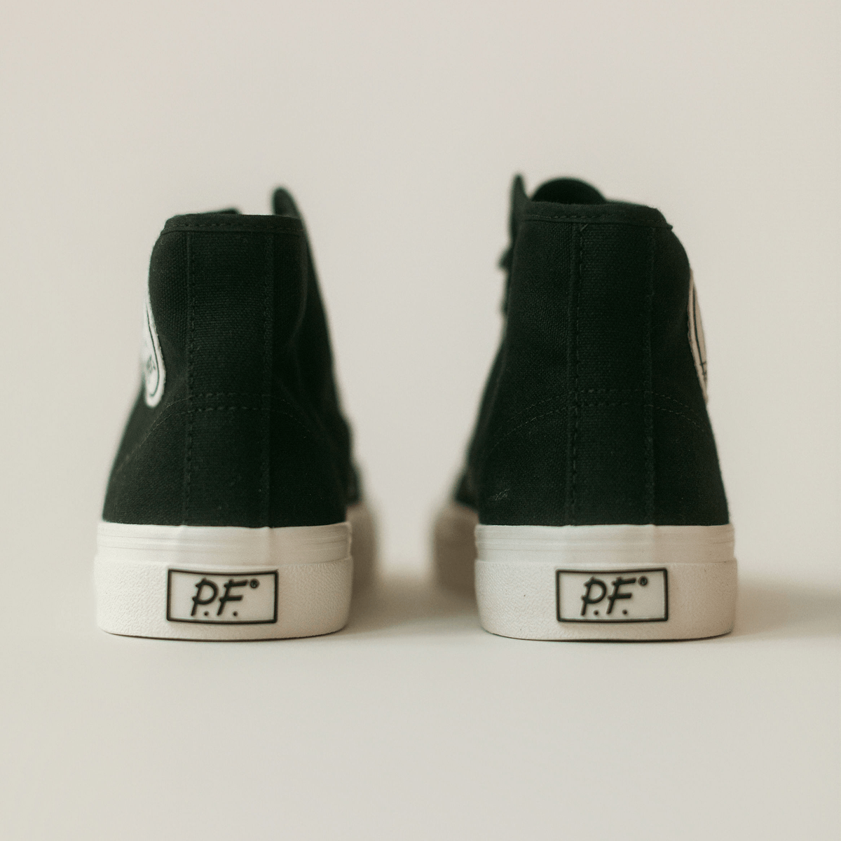 Rear view of black high-top sneakers with white soles on a light background.