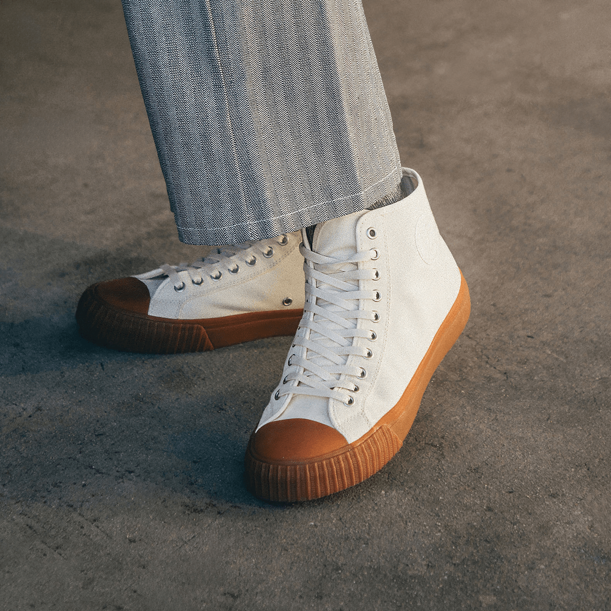 White high-top sneakers with brown soles worn by a person on a concrete floor.