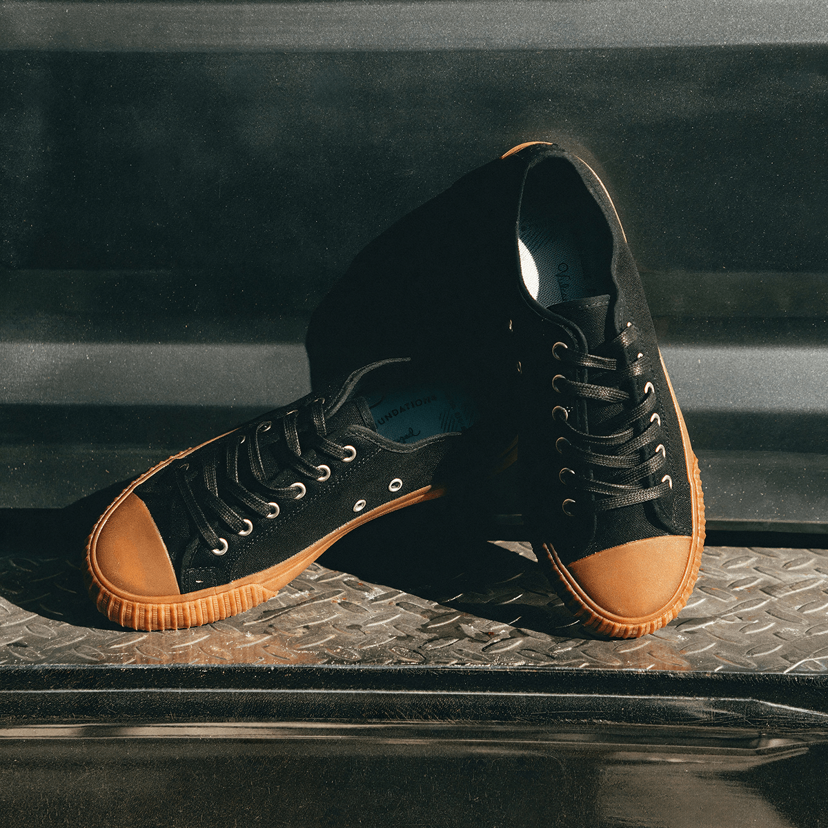 Black low-top sneakers with brown soles posed on a truck bumper.