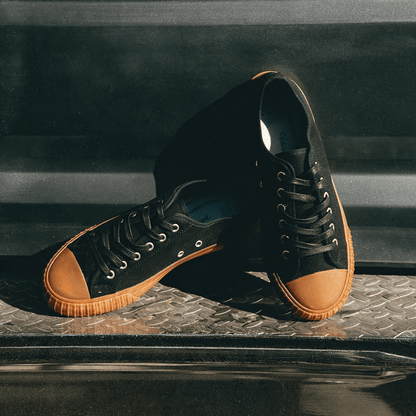 Black low-top sneakers with brown soles posed on a truck bumper.