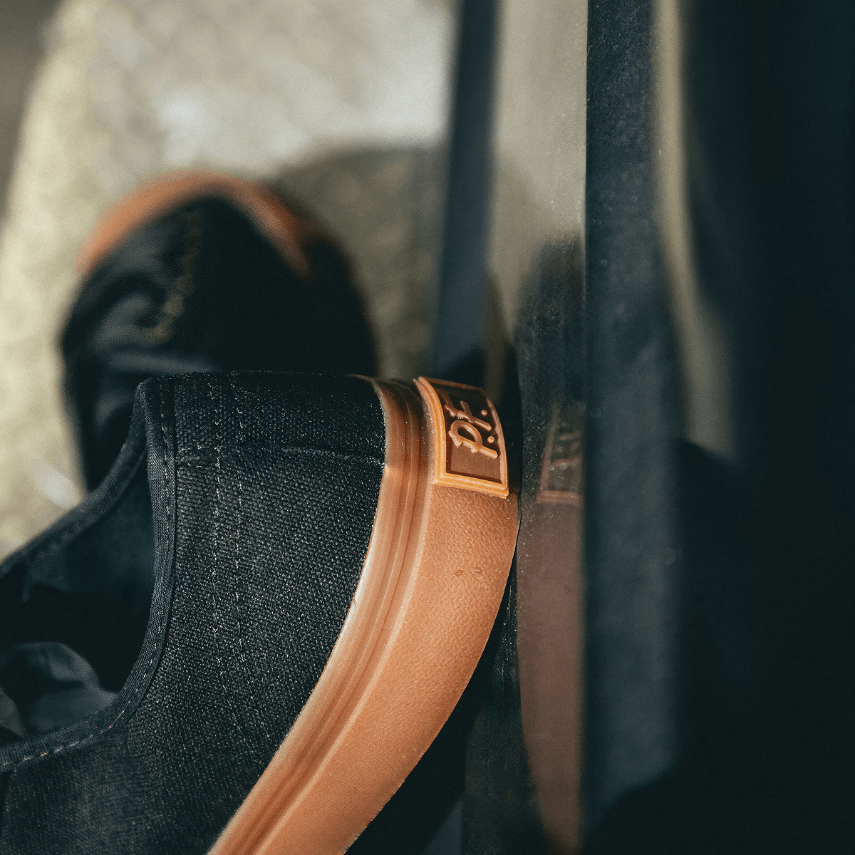 Close-up of a black low-top sneaker with a brown sole on a blurred background.