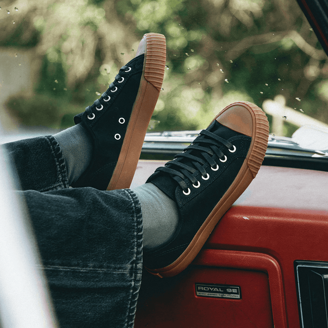 Person resting their feet on a red car dashboard while wearing black sneakers with brown soles.