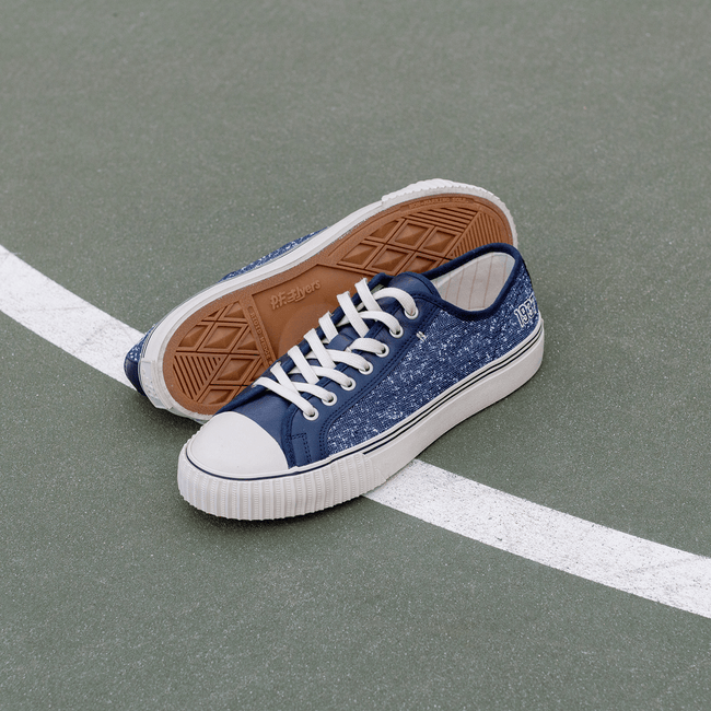 Blue navy low-top sneakers with white soles on a court.