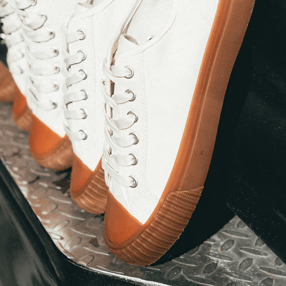 Close-up of white sneakers with brown soles on a truck bumper.