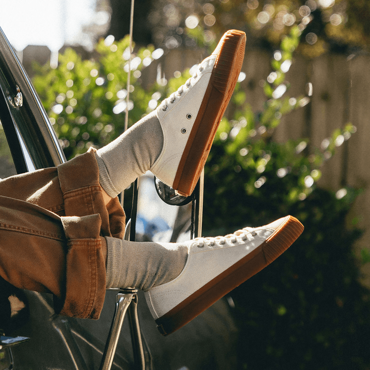 Person sitting in a car with their feet out the window, wearing white low-top sneakers with brown soles.
