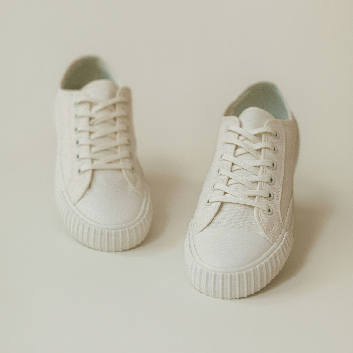 Pair of white low-top sneakers on a light background.