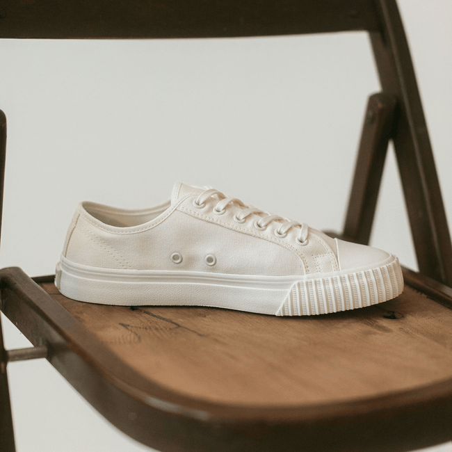 Close up of a white low-top sneaker on a wooden chair.