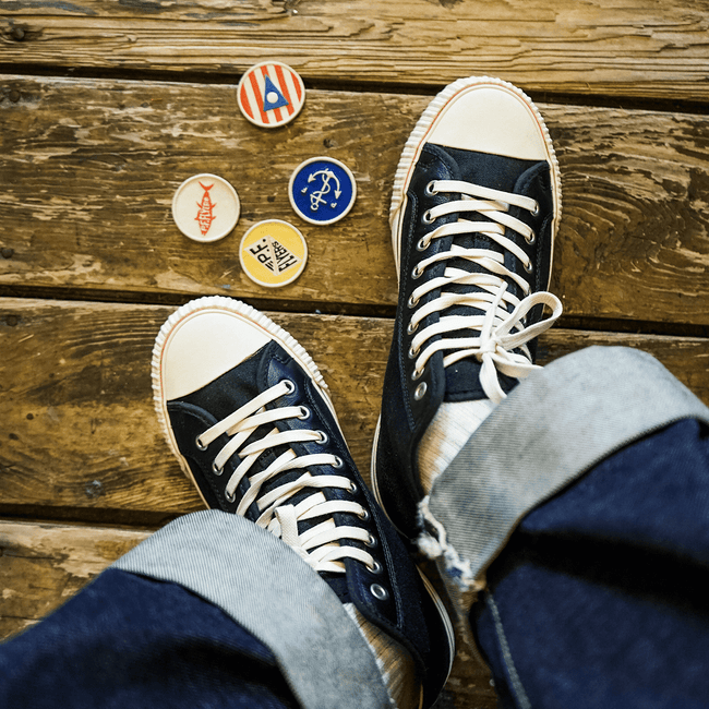 Black high-top sneakers with white laces on a wooden floor, with four colorful patches nearby.