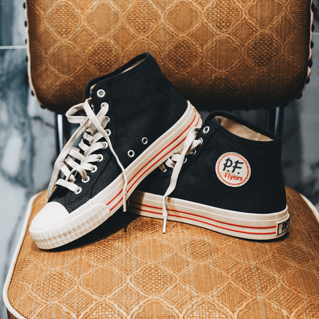Black high-top sneakers with red accents posed on a diner chair.