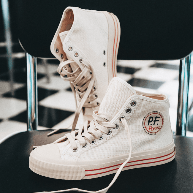 White high-top sneakers with red accents posed on a diner chair.