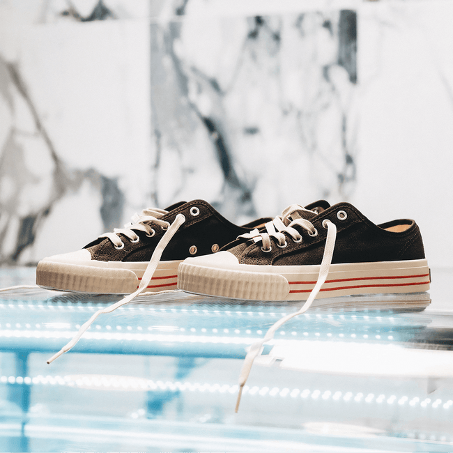 Pair of black low-top sneakers with white soles on a reflective surface.