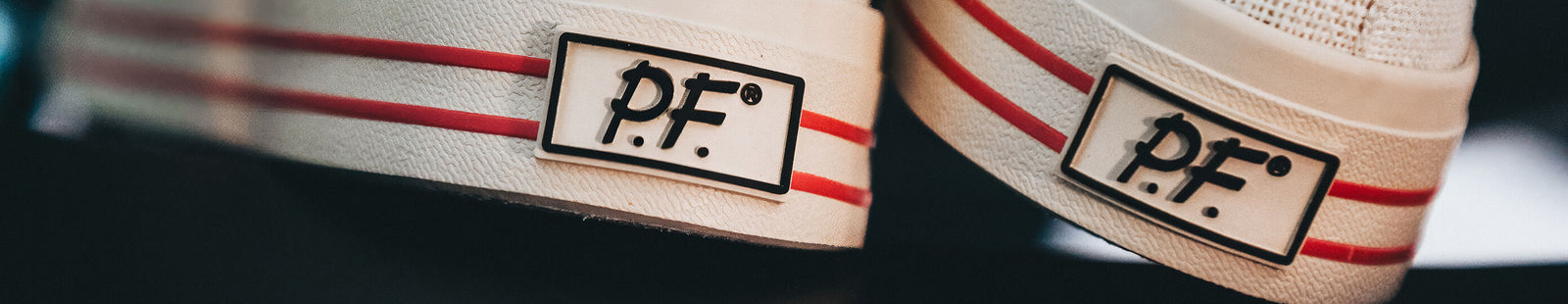 Close-up of white sneakers with red pinstripes and 'P.F.' branding on the heel.