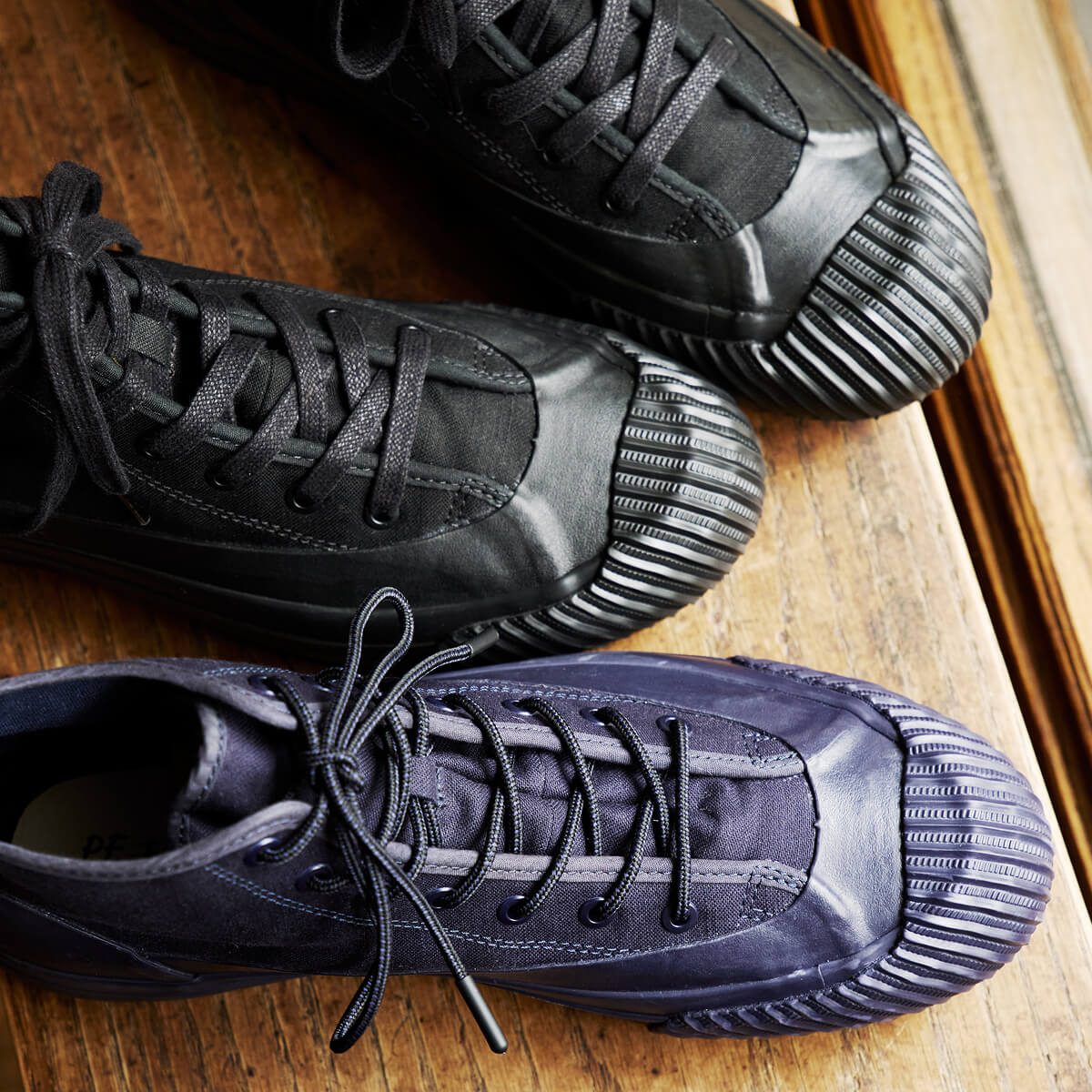 A pair of black boots with lugged rubber outsoles and flat hiker laces arranged on a wooden surface.