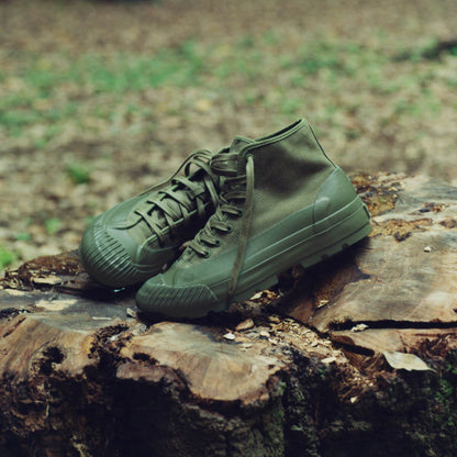 A pair of olive green canvas boots resting on a tree stump with a blurred forest background.